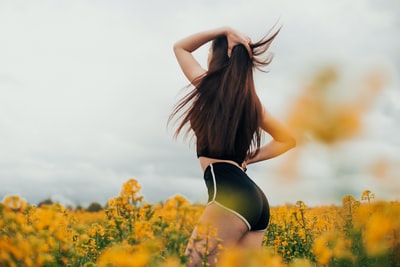 During the day, dressed in black and white striped bikini woman standing on the yellow flower bed
